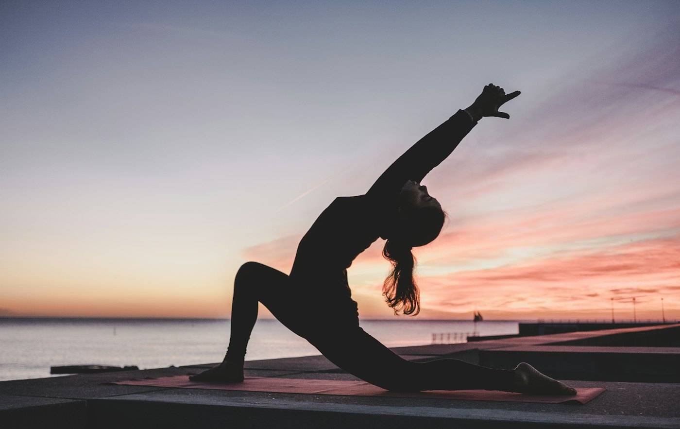 Persona practicando yoga frente al mar al atardecer